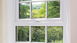 Una ventana blanca con múltiples divisiones, que ofrece vistas a un exuberante jardín verde.
