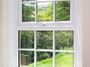 Ein weißes Fenster mit vielen Fensterscheiben, das einen Blick auf einen üppigen, grünen Garten freigibt.