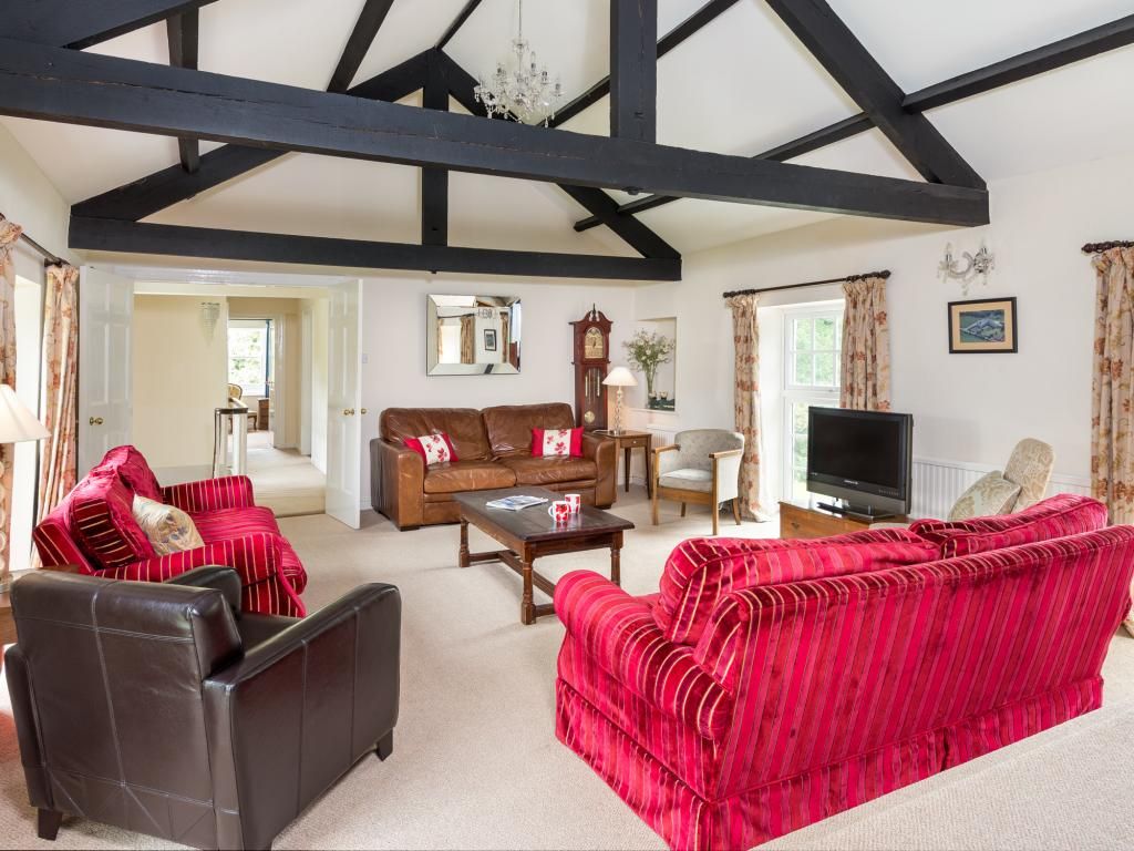 A living room with a high ceiling, exposed beams, a television, and a fireplace.