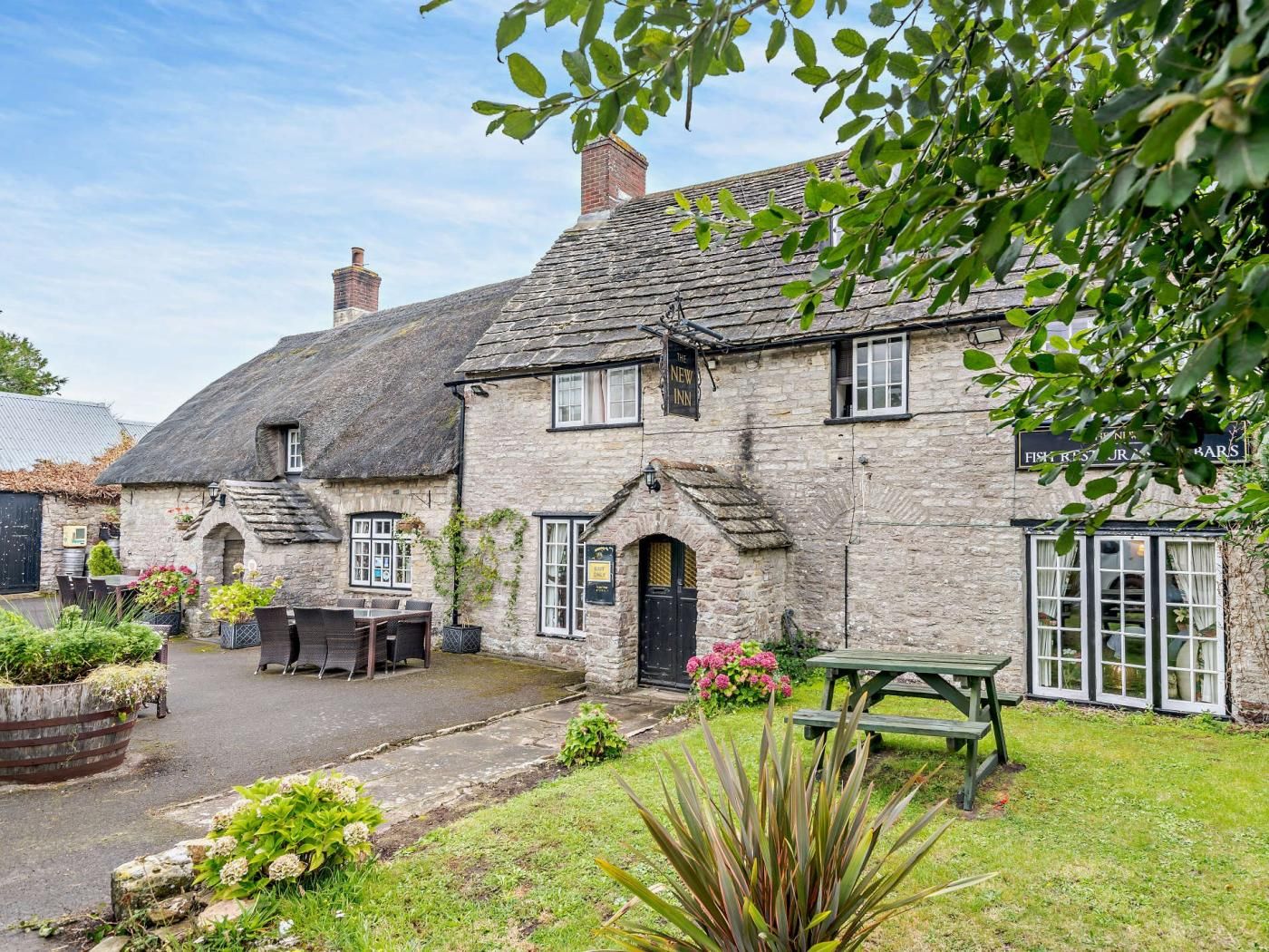 A stone building with a thatched roof, a sign for 'The New Inn,' and a visible outdoor seating area with tables and chairs.