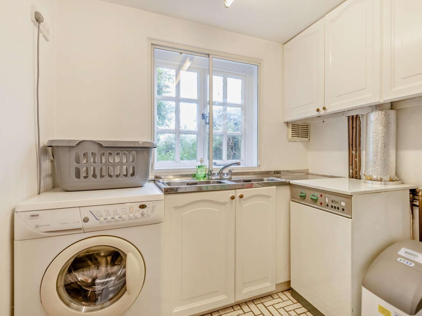 A compact laundry room with a washing machine, a drying rack, a sink, and a heater.