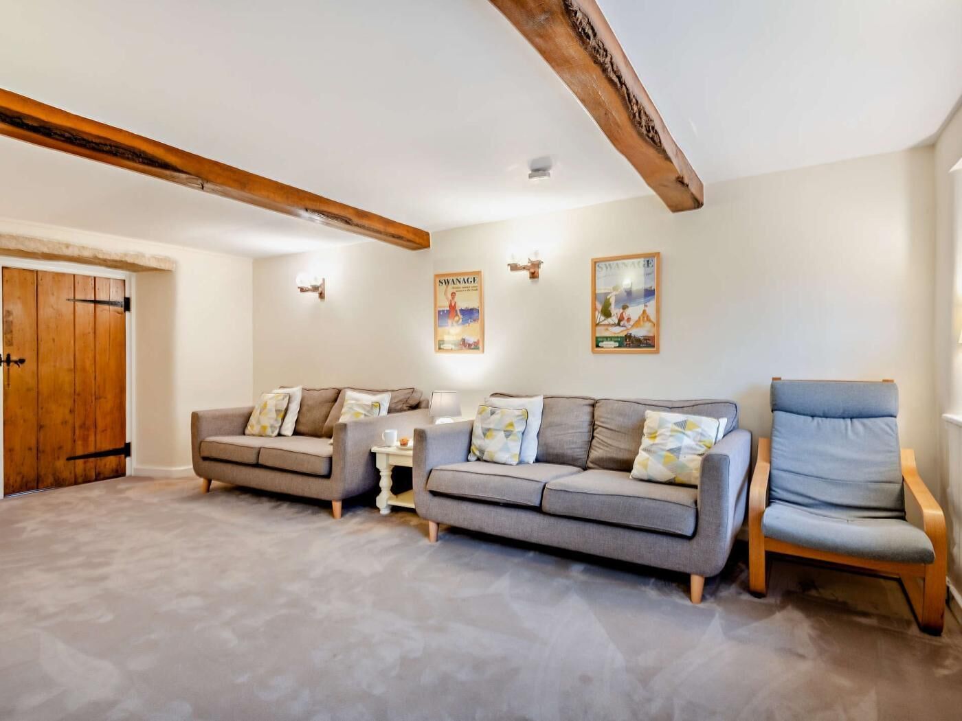 Een woonkamer met een zithoek, een stoel, een balkenplafond en een deur.