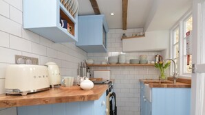 Una cocina con armarios azules, baldosas blancas, encimera de madera, un tostador, un hervidor y un fregadero.