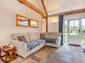 A cozy living room with a stone floor, a wooden-framed ceiling, a large mirror, and a door leading outside. - 2 Bed in Wareham (oc-dc184) (Stoborough)