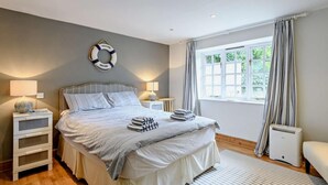 Un dormitorio con cama, mesitas de noche, un salvavidas colgado en la pared, una ventana con cortinas y un radiador.