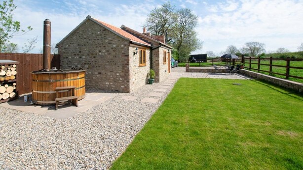 A stone building with a chimney, a wooden barrel, and a gravel path leading to a grassy area. - 1 Bed in Darlington (oc-75147) (Stapleton)