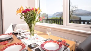 Une table à manger dressée avec des assiettes, des couverts et un vase de fleurs, offrant une vue pittoresque sur un lac.