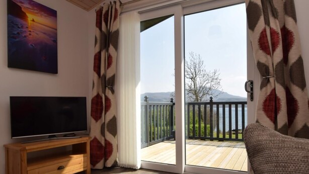 Un salon comprenant un téléviseur, un canapé, un meuble TV en bois et une porte-fenêtre coulissante donnant sur une terrasse extérieure.