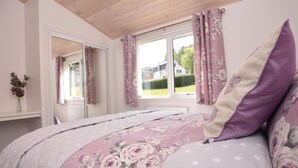 Une chambre à coucher avec un lit, des rideaux à motifs floraux, une fenêtre donnant sur un beau paysage et un miroir.