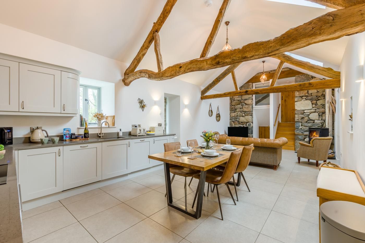 A spacious kitchen with white cabinets, a dining table set for four, and a stone fireplace.