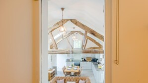Ein Zimmer mit hoher Decke, freiliegenden Holzbalken, einer Essecke mit Tisch und Stühlen und Blick durch ein Fenster.
