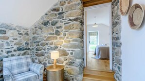 A stone-walled room with a plaid sofa, a lamp, and a bed in the background. - 3 Bed in Llwyngwril (oc-75025) (Llwyngwril)