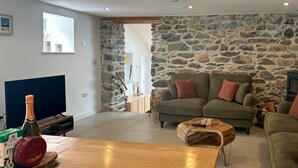A living room with a stone wall, a sofa, a coffee table, and a television. - 3 Bed in Llwyngwril (oc-75025) (Llwyngwril)