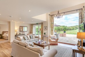 A spacious living room with a sofa set, a coffee table, and a chair. There is a large window with curtains, a chandelier, and a view of the outdoors. - 3 Bed in Dorchester (oc-75244) (Sydling Saint Nicholas)