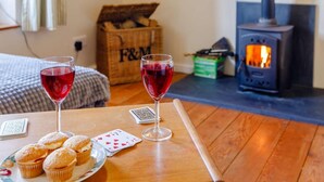 Una stanza accogliente con un tavolo di legno, due bicchieri di vino rosso, un piatto di muffin, carte da gioco e un camino ben visibile.