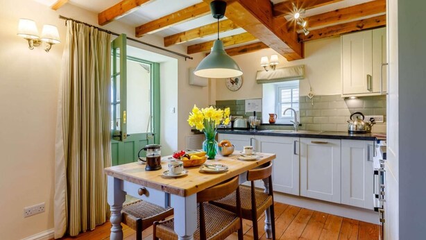 Una cucina con travi in legno, un tavolo da pranzo con sedie, un bollitore e un vaso con fiori.