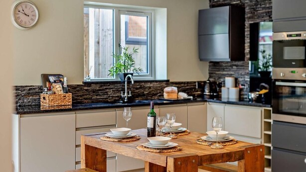 Uma cozinha moderna com mesa de madeira posta para refeições, janela com vista e eletrodomésticos embutidos.