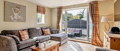A living room with a sofa, a coffee table, and a lamp. There is a window with curtains and a view of the outside.
