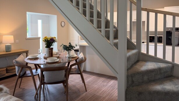Ein Essbereich mit Tisch für vier Personen, einer Treppe und einer Küche im Hintergrund.