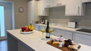 Eine moderne Küche mit weißen Schränken, einer Obstschale, Weingläsern und einem Käsebrett.