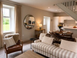A living room with a sofa, armchair, and a dining table set for four. - Greenkeepers Cottage (Tobermory)