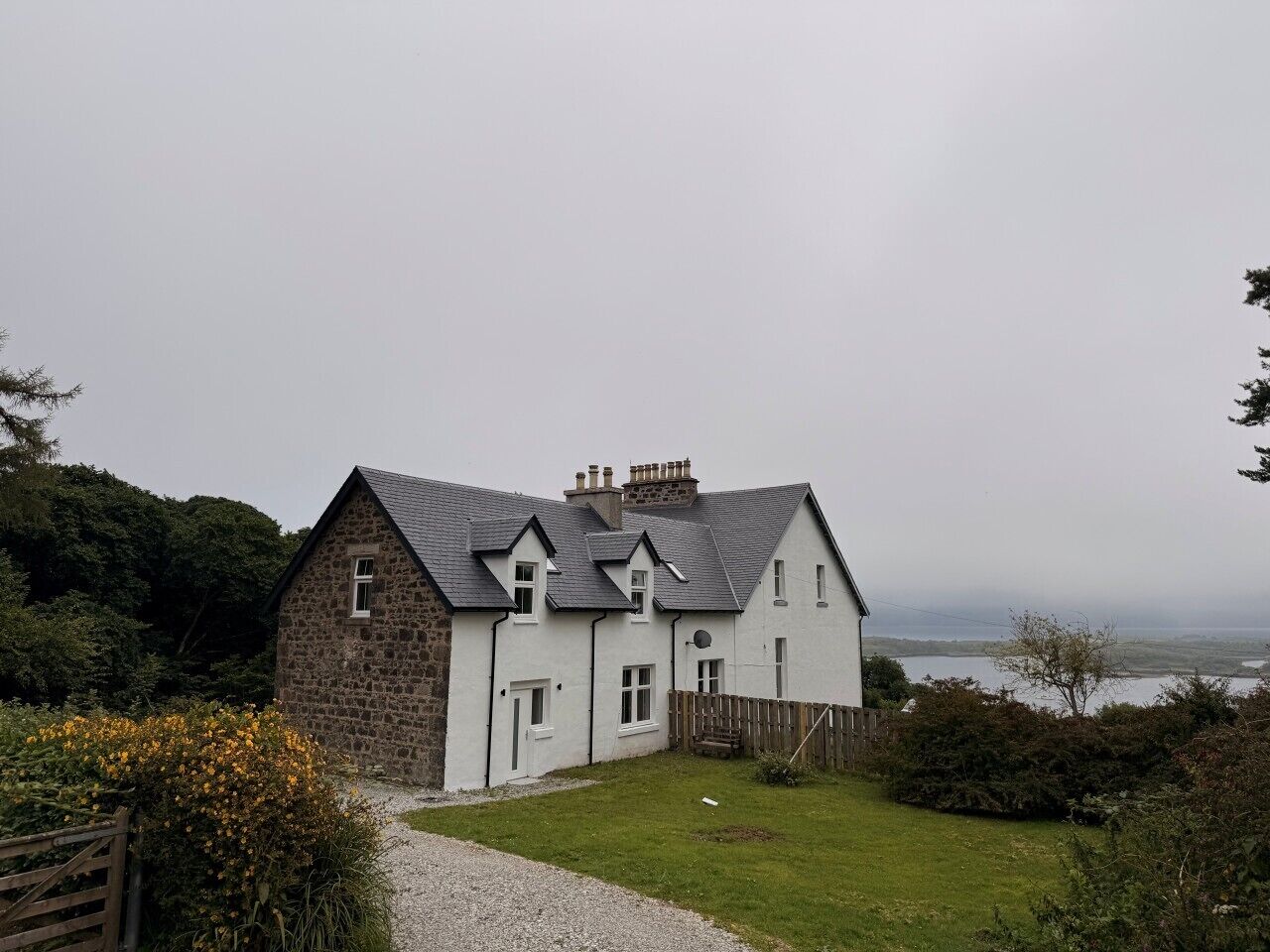 Una casa de piedra de dos pisos con fachada blanca, techo gris y vista al mar.
