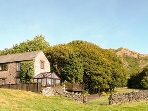 A stone house with a glass conservatory, surrounded by a stone wall and a wooden gate. - 3 Bed in Eskdale (oc-sz502) (Eskdale)