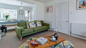 A living room with a green sofa, a wooden coffee table, and a dining area with a table set for two. - 3 Bed in Norwich (oc-75160) (Mundesley)