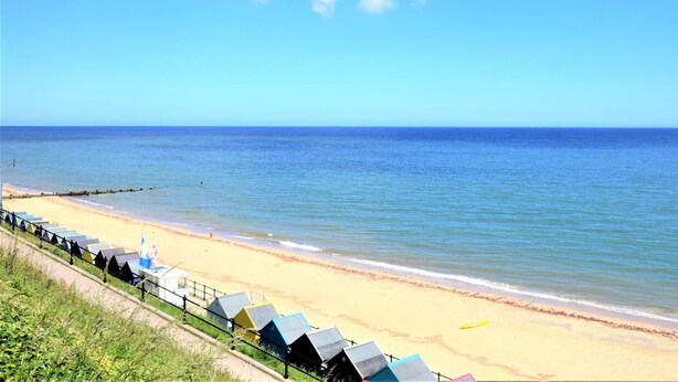 A beach with a row of colorful beach huts along the shore. - 3 Bed in Norwich (oc-75160) (Mundesley)
