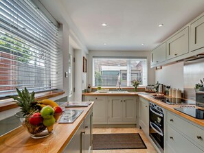 Eine moderne Küche mit Holzarbeitsplatte, einer Obstschale, einem Fenster mit Jalousien und einem eingebauten Backofen.