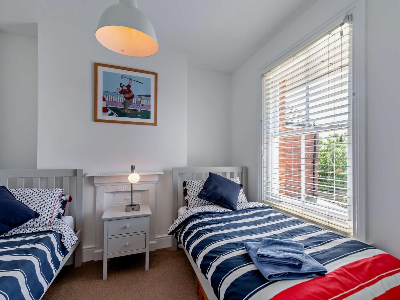 A bedroom with two beds, a nightstand, a lamp, a framed picture, and a window with blinds.