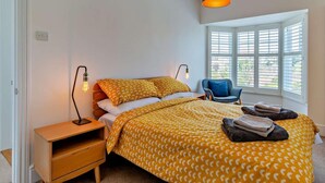 A bedroom with a bed, bedside tables, a chair, a window with blinds, and a hanging light fixture. - 3 Bed in Norwich (oc-75160) (Mundesley)