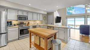 A modern kitchen with white cabinets, stainless steel appliances, a wooden island, and a view of the ocean. - Lakefront Townhome | Private Boat Slip | Swim + Fish | Pool Access | Near Ren Fest | Sleeps 8 (Montgomery)