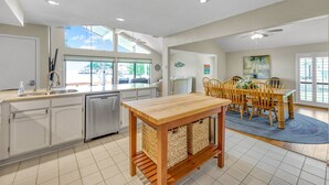 A modern kitchen with a dishwasher, a dining area with a wooden table and chairs, and a large window providing natural light. - Lakefront Townhome | Private Boat Slip | Swim + Fish | Pool Access | Near Ren Fest | Sleeps 8 (Montgomery)