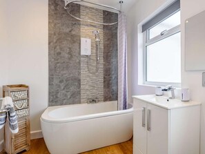 Ein modernes Badezimmer mit einer freistehenden Badewanne, einer Dusche, einem Fenster und einer Holzaufbewahrungseinheit.