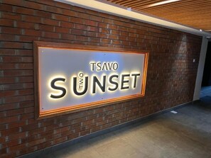 En skylt med texten ”TSAVO SUNSET” på en tegelvägg.