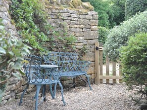 A stone wall, a metal bench, and a wooden gate in a garden. - 3 Bed in Cheltenham (oc-75532) (Bourton-on-the-Water)