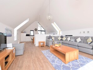 Ein modernes Loft mit Essbereich, einem Wohnzimmer mit grauem Sofa und einer Küche im Hintergrund.
