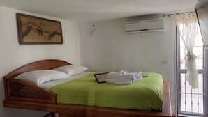 Una cama individual con una colcha verde, almohadas blancas y una obra de arte enmarcada sobre ella.