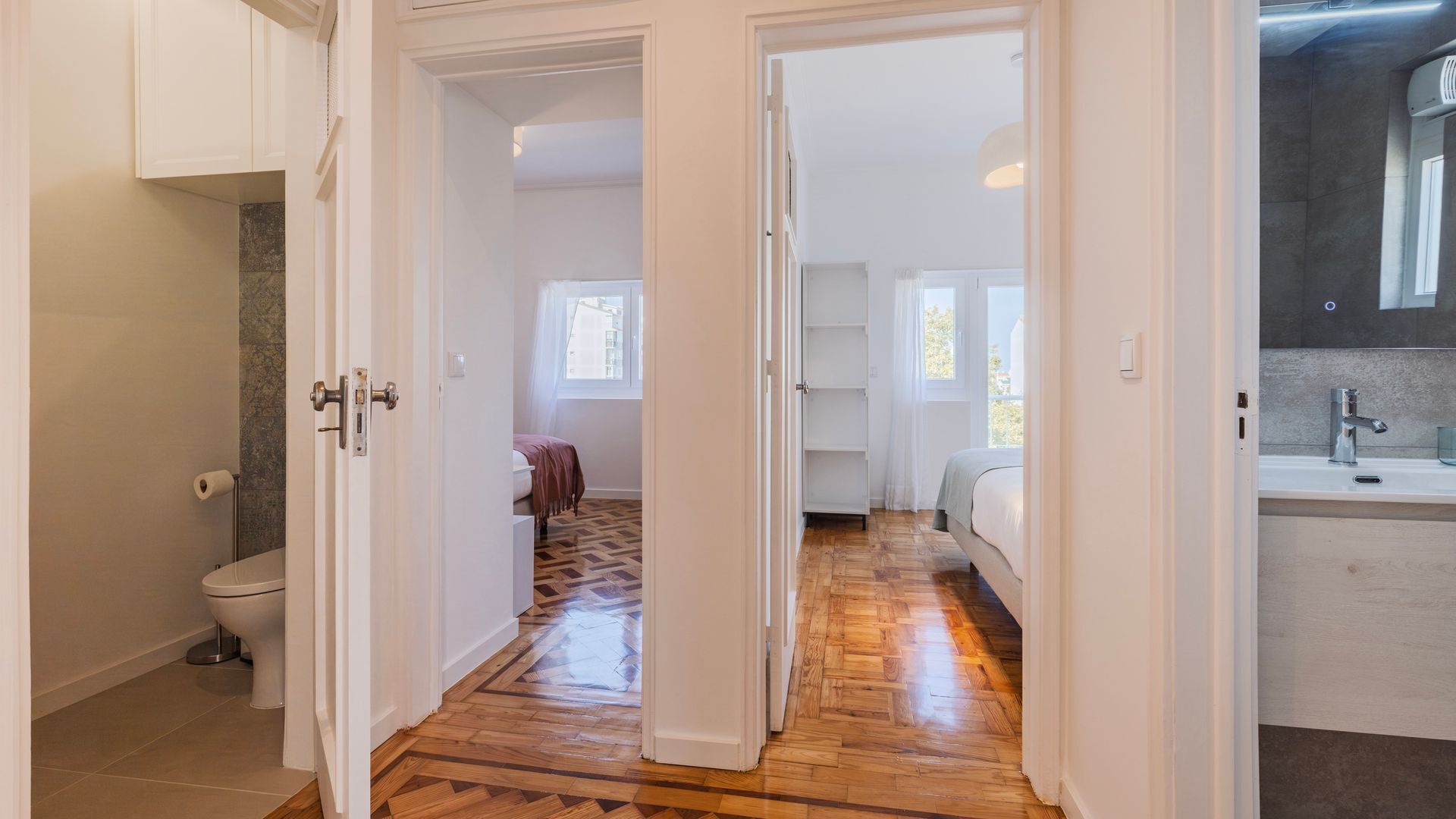 A hallway leading to a bedroom with a wooden floor, a bathroom with a toilet, and a kitchen area with a sink and countertop.