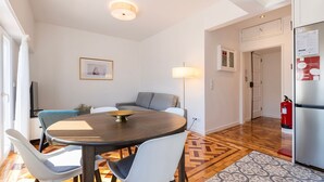 Moderni keittiö, jossa on jääkaappi, ruokailutila pyöreällä pöydällä ja tuoleilla, sohva, lamppu ja seinällä oleva kehystetty taulu.