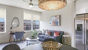 Ein modernes Wohnzimmer mit Sofa, Couchtisch und Esstisch. Es gibt eine Küchenzeile mit Kühlschrank sowie eine Essecke mit Stühlen.