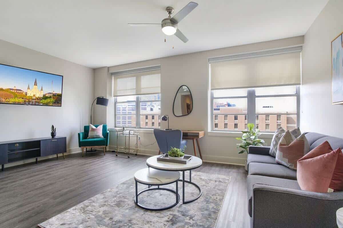 Una sala de estar moderna con un sofá, un sillón, una mesa redonda y ventanas amplias.