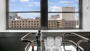Ein Fenster mit Blick auf die Stadt, eine Bar mit Cocktailshaker und Gläsern sowie ein Tablett.