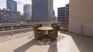 Eine Dachterrasse mit einem runden Tisch und Korbstühlen, mit Blick auf eine Skyline mit Hochhäusern.