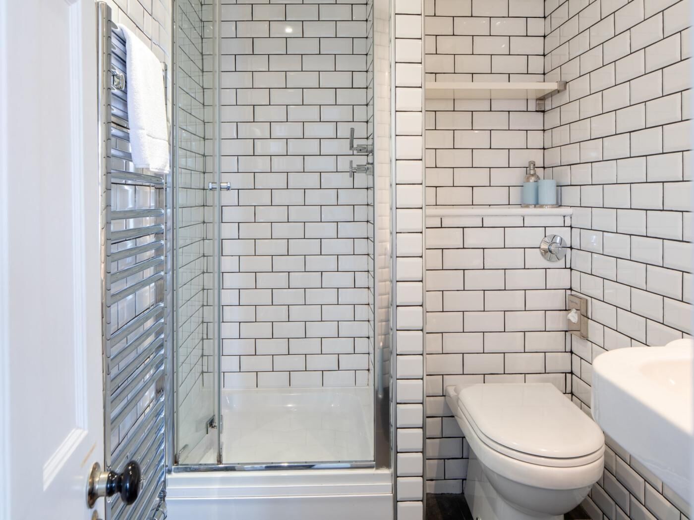 Une salle de bain avec des carreaux de céramique blancs rectangulaires, une douche en verre, des toilettes et un lavabo.