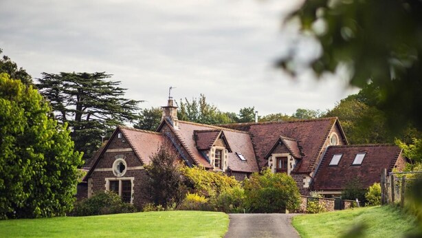 A traditional stone house with multiple gabled roofs, a central chimney, and a paved driveway leading to the entrance. - 5 Bed in Worcester (oc-75602) (Halmond's Frome)