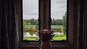 A window with a view of a lake and greenery, a vase with flowers on a table in front. - 1 Bed in Worcester (oc-75600) (Halmond's Frome)