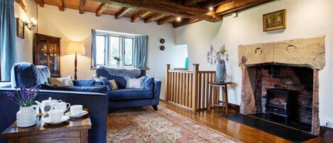A cozy living room with a fireplace, wooden beams, a blue sofa, and a patterned rug.