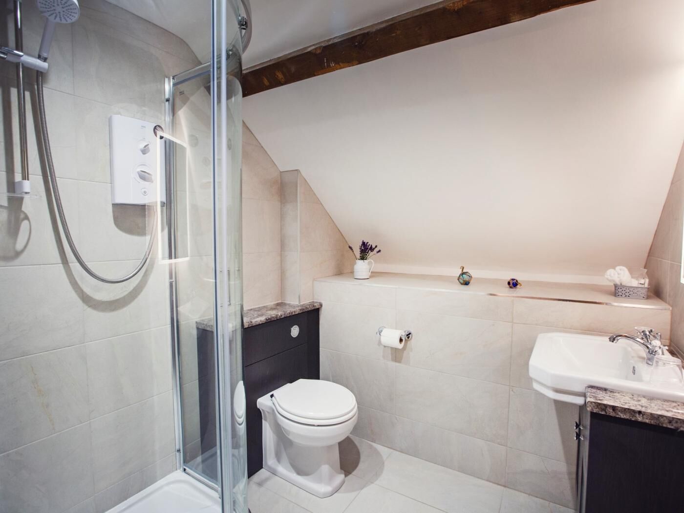 Ein modernes Badezimmer mit einer Duschkabine aus Glas, einer Toilette, einem Waschbecken und einer kleinen Ablagefläche mit Pflegeprodukten.